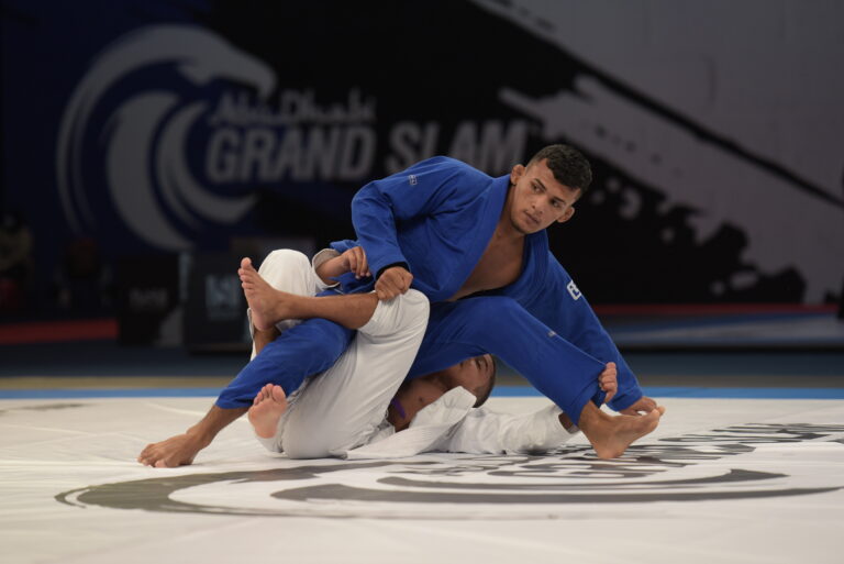 Dois atletas de jiu-jitsu, com quimonos azul e branco, durante uma luta.